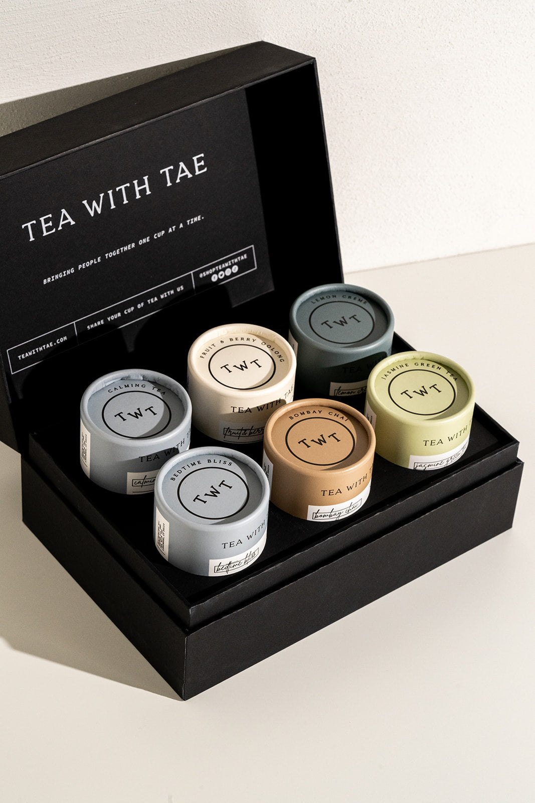 Black Tea With Tae gift box opened to display six mini tea tubes in assorted flavors on a white surface.
