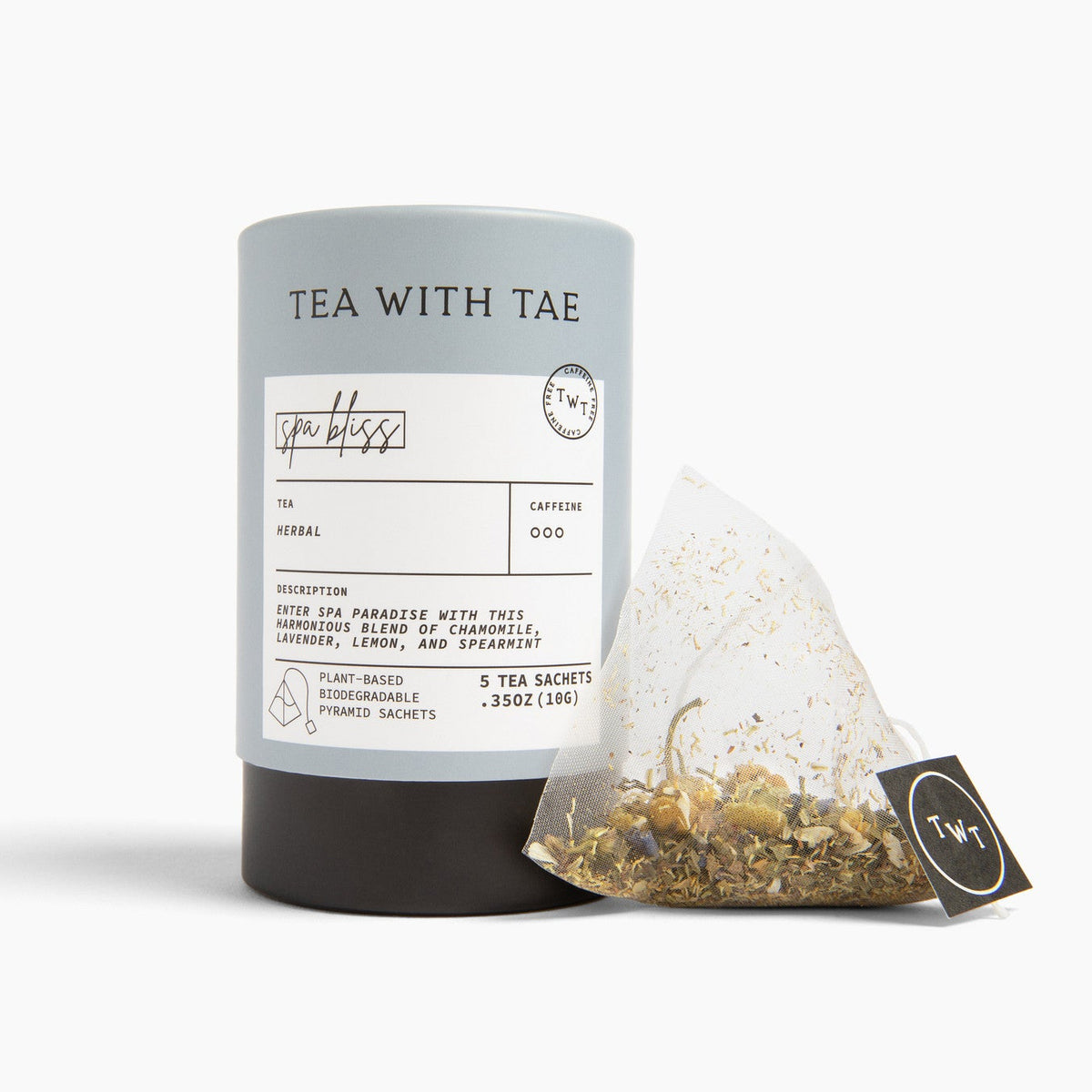 A blue cylindrical tea tube labeled 'TEA WITH TAE' stands on a white studio background next to a single triangular tea bag with a black tag.