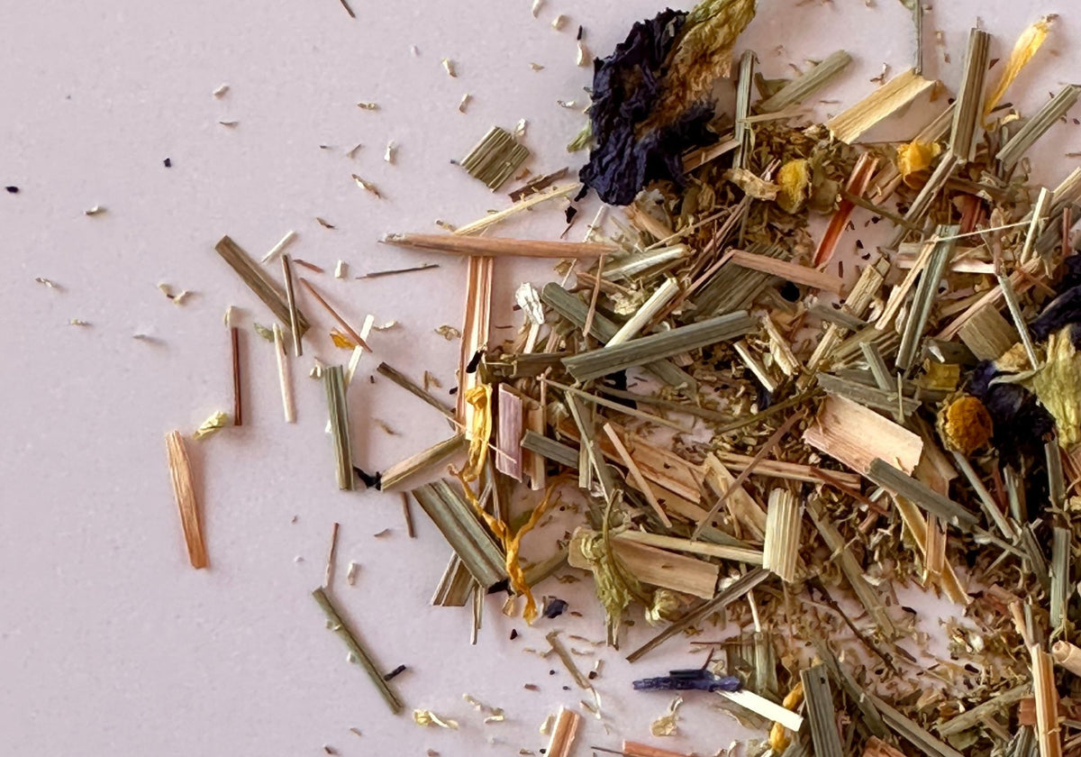 Close-up of loose leaf tea blend with dried herbs, lemongrass pieces, flower petals, and botanical ingredients on a light surface.