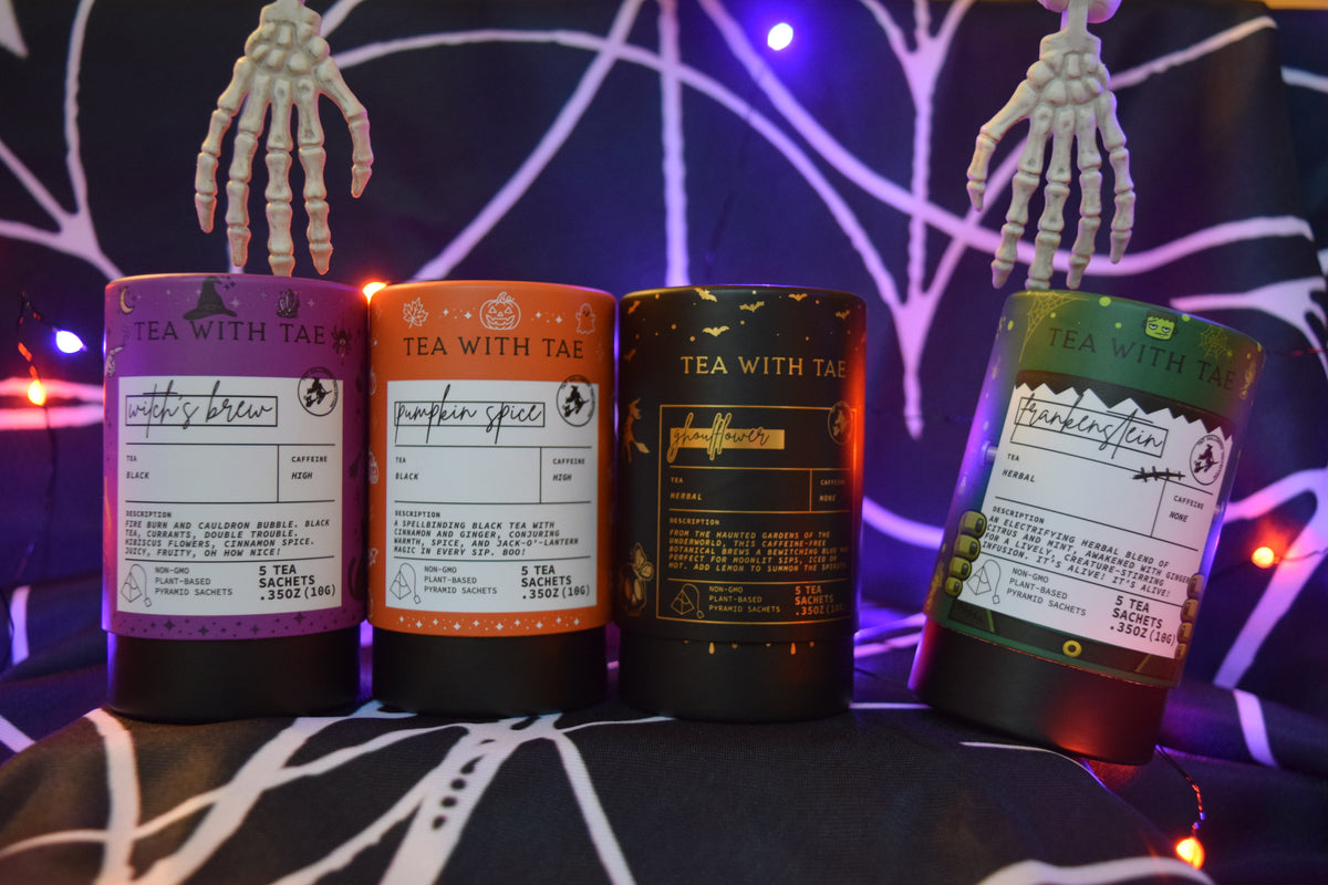 Four cylindrical tea tins with Halloween-themed labels are lined up on a black surface with spiderweb lighting and skeleton hands above them. The labels read 'TEA WITH TAE' and show flavors including Witch's Brew, Ghoulflower, Pumpkin Spice, and Frankenstein.