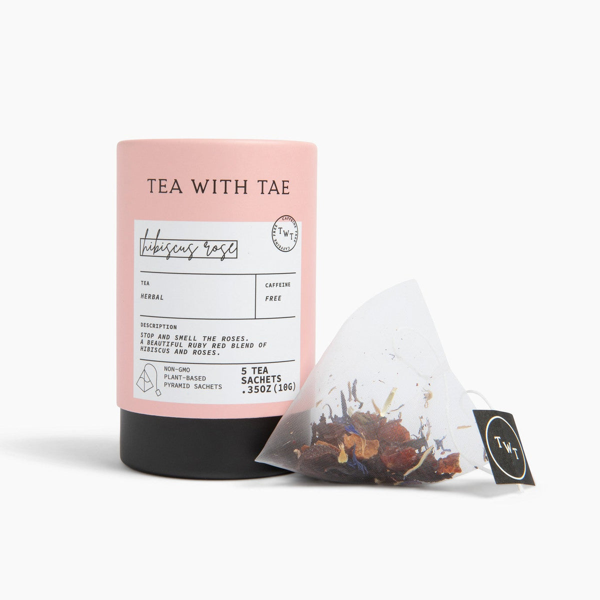 A pink cylindrical tea tube labeled 'TEA WITH TAE' stands on a white studio background next to a single triangular tea bag with a black tag.