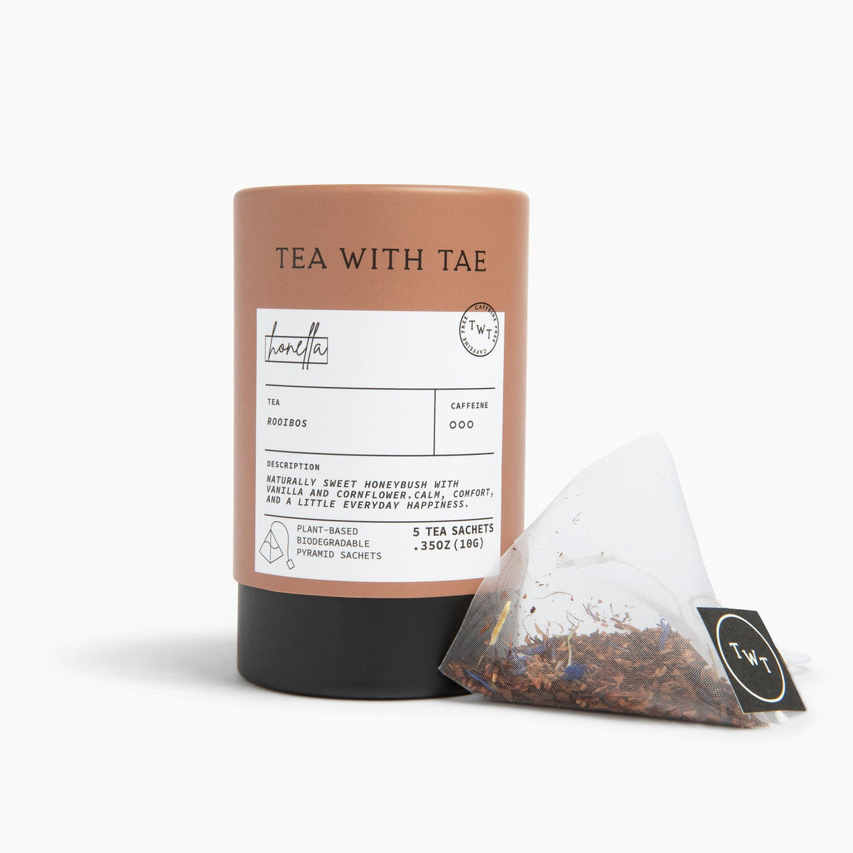 A brown cylindrical tea tube labeled 'TEA WITH TAE' stands on a white studio background next to a single triangular tea bag with a black tag.