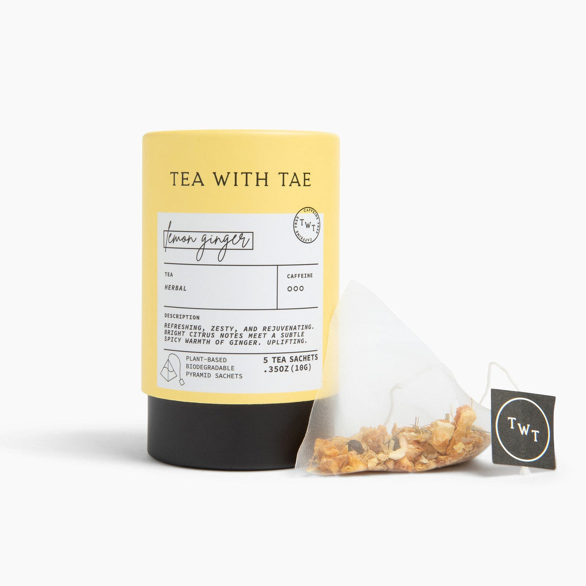 A bright yellow cylindrical tea tube labeled 'TEA WITH TAE' stands on a white studio background next to a single triangular tea bag with a black tag.